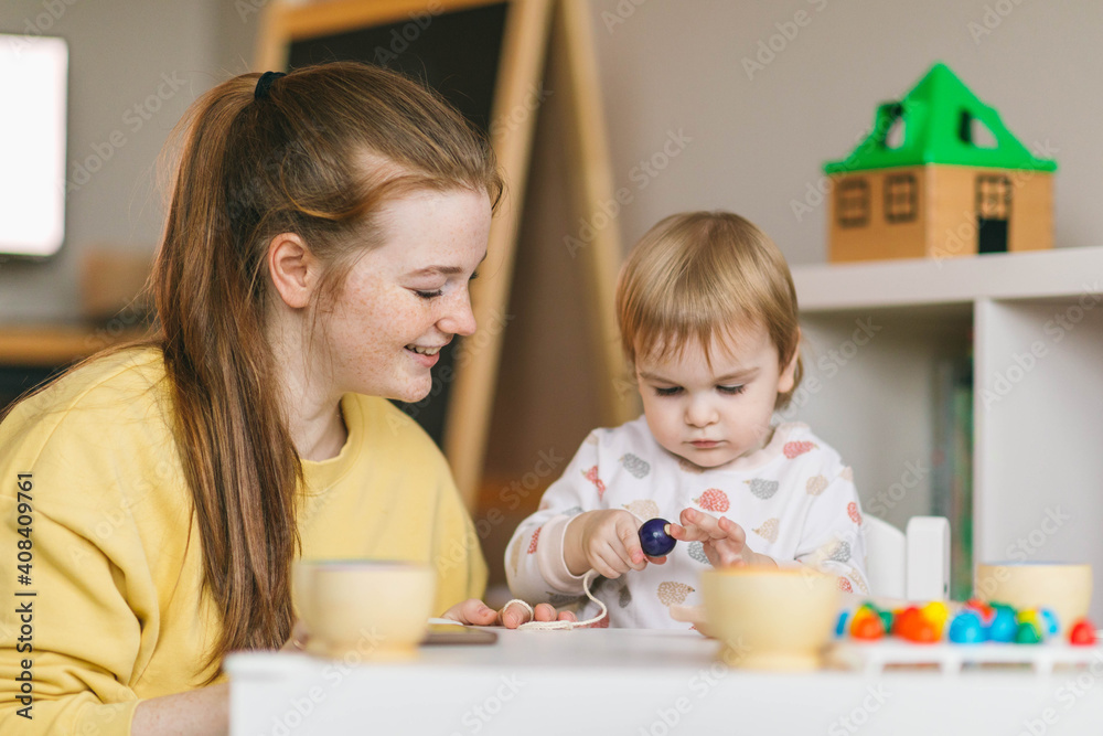 Early childhood learning. Mother and child play with wooden beads and cups, teaching colors and developing fine motor skills