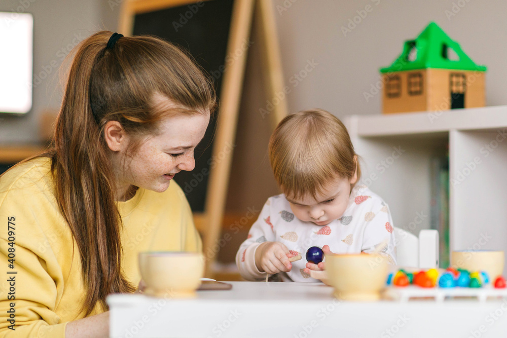 Fototapeta premium Early childhood learning. Mother and child play with wooden beads and cups, teaching colors and developing fine motor skills