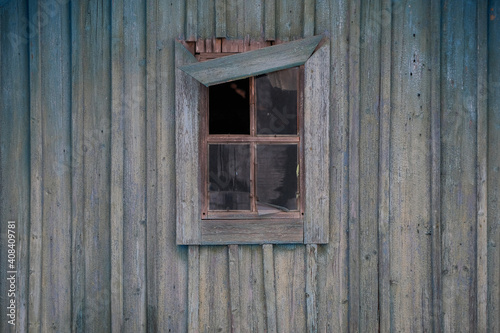 A small wooden window with broken glass and a rickety skirting board against the old wooden wall.