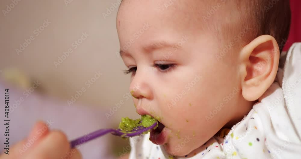 mother holds the baby in her arms and feeds her boy with a spoon. family, food, child, eating and parenthood concept mother holds the baby in her arms and feeds her boy with a spoon. family, food, child, eating and parenthood concept