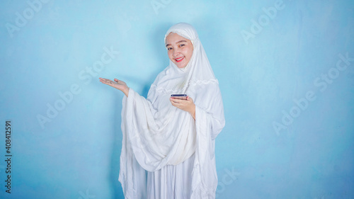 attractive asian muslim woman presenting and holding smartphone. free copy space isolated over blue background