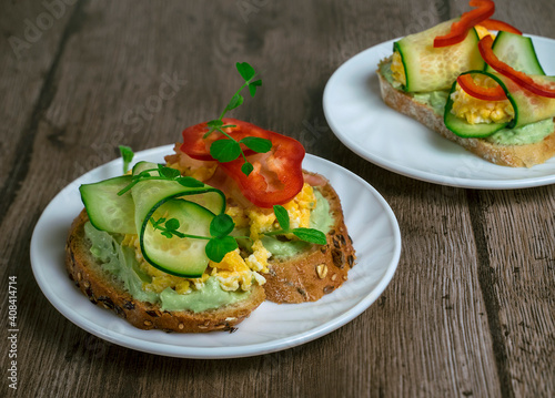 healthy snack, sandwiches with cereal bread, avocado cream, scrambled eggs and cucumber on a wooden table