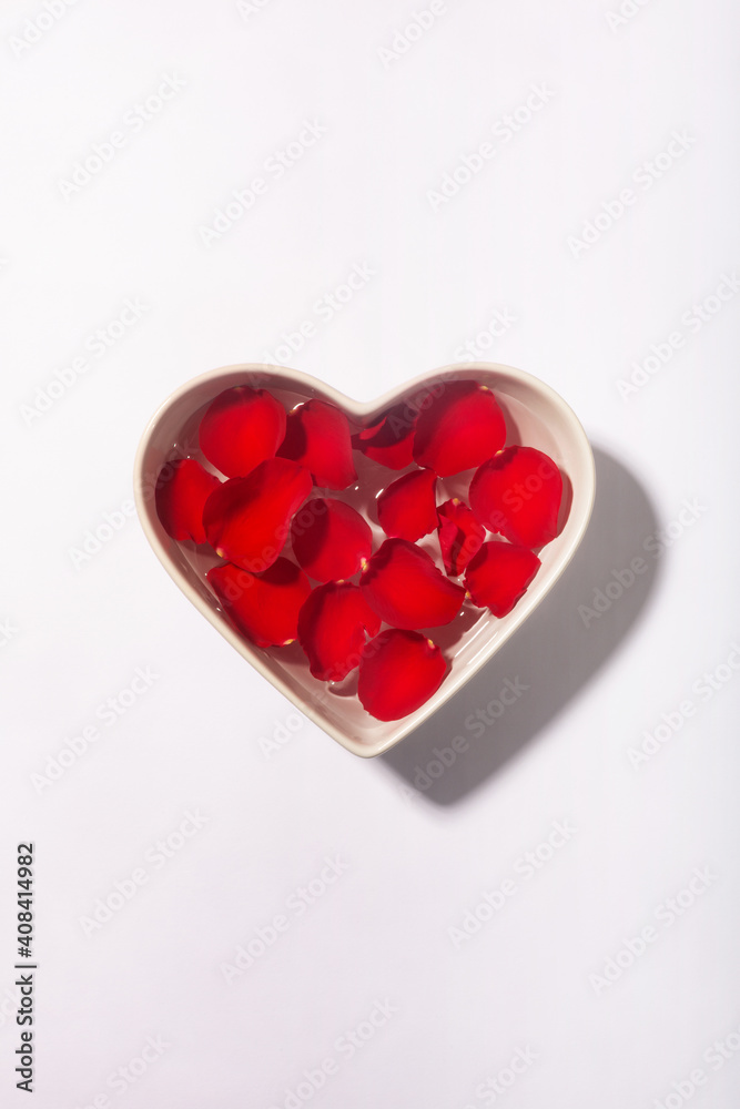 White heart shaped bowl with red rose petals on the water surface