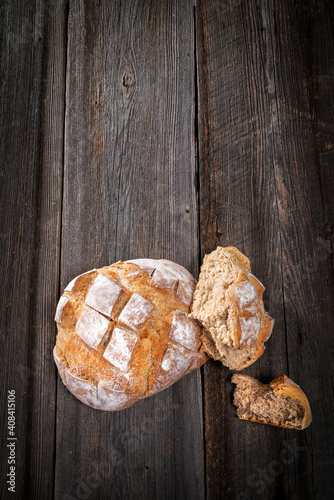 Country bread with floured crust with pieces on a barn wood board on white background