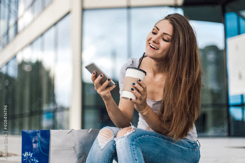 Woman using phone sitting near mall with coffee after shopping.