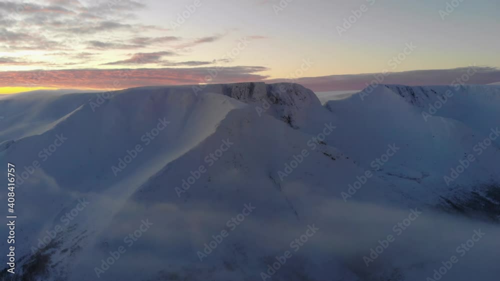 Flying over the clouds to a snowy mountain at sunset. Aerial view. Flying over the clouds to a snowy mountain at sunset. Aerial view.
