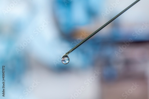 Syringe needle with a drop of serum on top. Blurred background that is reflected in the serum drop.
