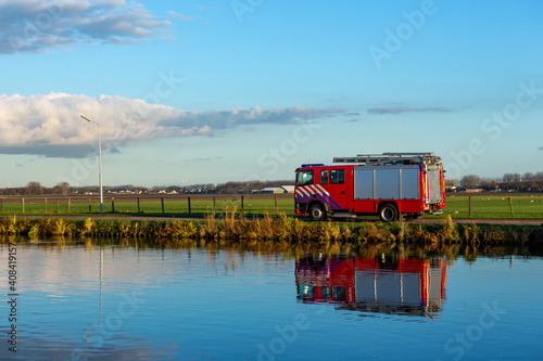 A red firetruck driving on the Lisserdijk along the river the Ringvaart in the village of Lisse in the Province of North-Holland in the Netherlands. photo