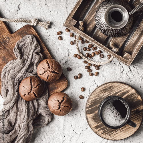 Coffee beans with coffee and muffins on grey textured background.