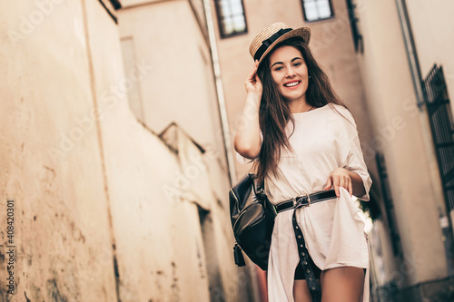 Young stylish woman walking on the old town street, travel with backpack, straw hat, wearing trendy outfit. © zadorozhna