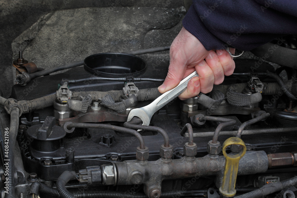 Worker fixing modern common rail diesel engine, closeup of hand with spanner tool, rail, pipeline and injectors