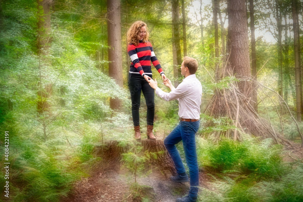 A young man in love helps the woman off a tree trunk in the forest. background blurred A young man in love helps the woman off a tree trunk in the forest. background blurred