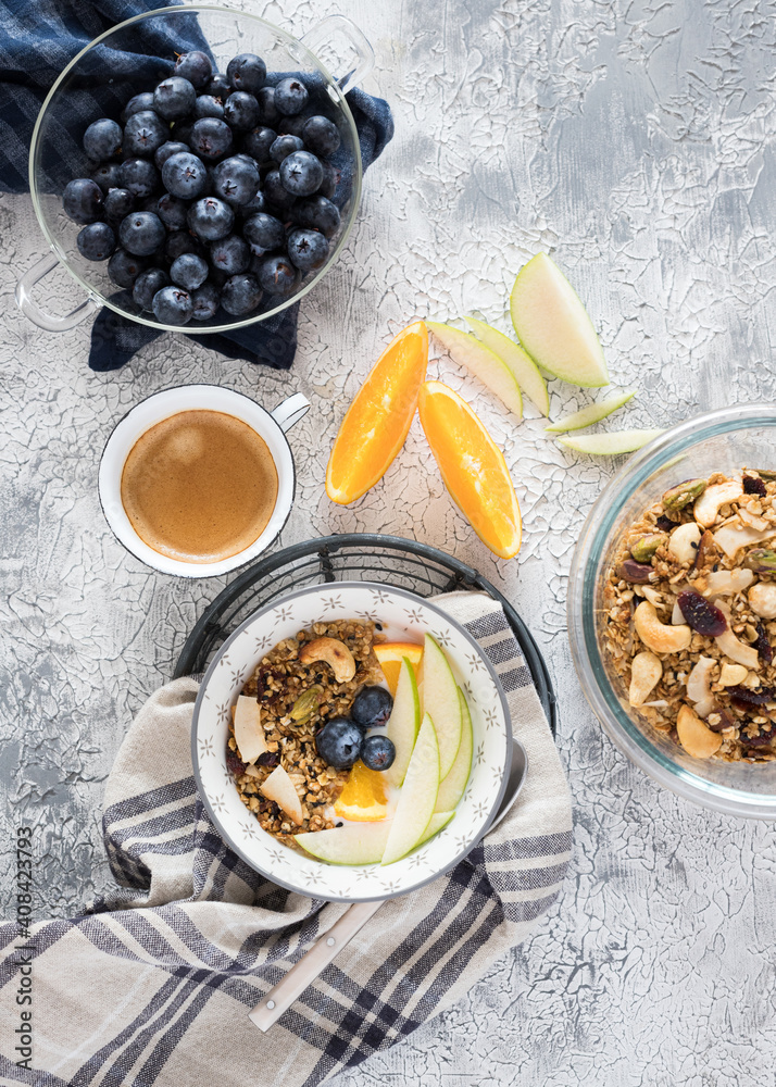 Overhead view of two granola bowls next to a foamy coffee cup, some orange and apple slices in the middle and a glass jar full of fresh cranberries.