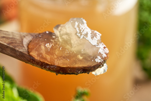 Chilled jellied beef bone broth on a spoon, with a glass jar full of broth in the background photo