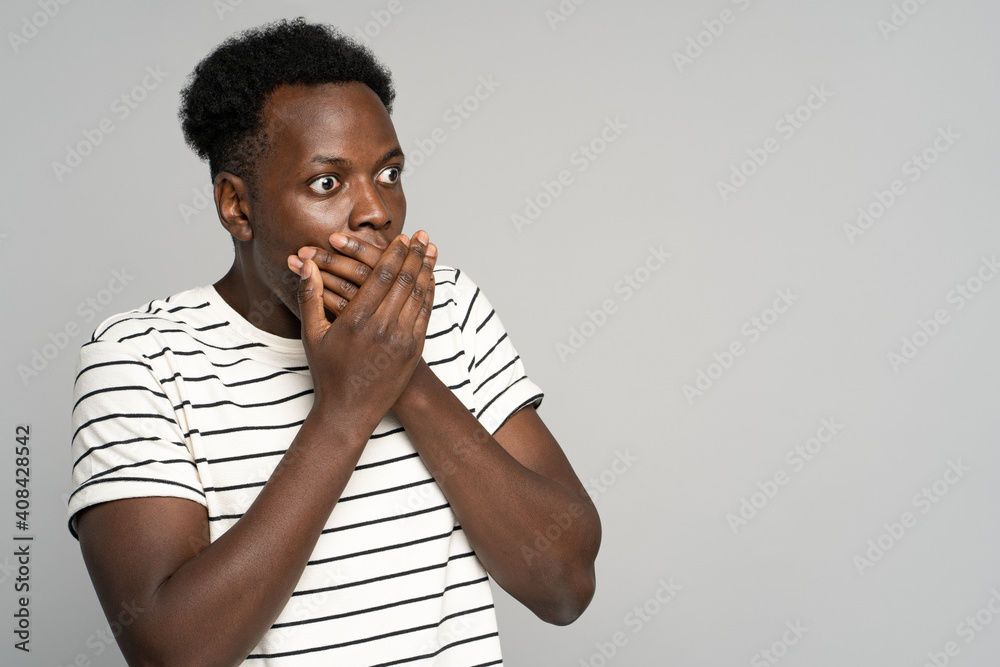 Surprised young afro man wear stripped t-shirt makes big eyes opens, covering mouth with hands, shocked with unprecedentedly low prices, sale, looking at copy space, isolated on studio grey background Surprised young afro man wear stripped t-shirt makes big eyes opens, covering mouth with hands, shocked with unprecedentedly low prices, sale, looking at copy space, isolated on studio grey background