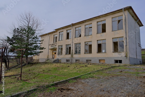 07.01.2021. Bulgaria, Kardzali. Old brownfield and abandoned soviet type school with overcast and very cloudy sky. School inside the green grass with broken windows. photo