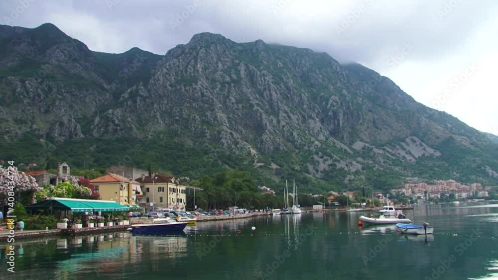 Sea coast town in Boka Kotorska Bay in Montenegro. Boats, marine, clear sea water, mountain and dark clouds. Sea coast town in Boka Kotorska Bay in Montenegro. Boats, marine, clear sea water, mountain and dark clouds.