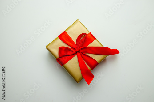 A holiday gift. Box in a gold gift wrapping with a red bow, on a white background. Merry Christmas, Happy New Year and Valentine's Day greetings. Postcard. High quality photo