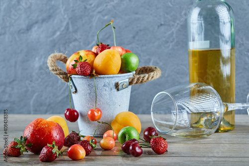 Bucket of fresh summer fruits  bottle of white wine and empty glass on wooden table