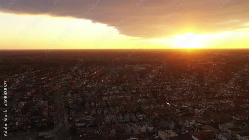 A high angle, aerial view over a Long Island neighborhood during a golden sunrise. It was shot with a drone which dolly out and pan right as it faces the sun and the dark clouds.