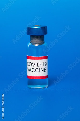 Vial filled with Covid-19 vaccine on blue background.