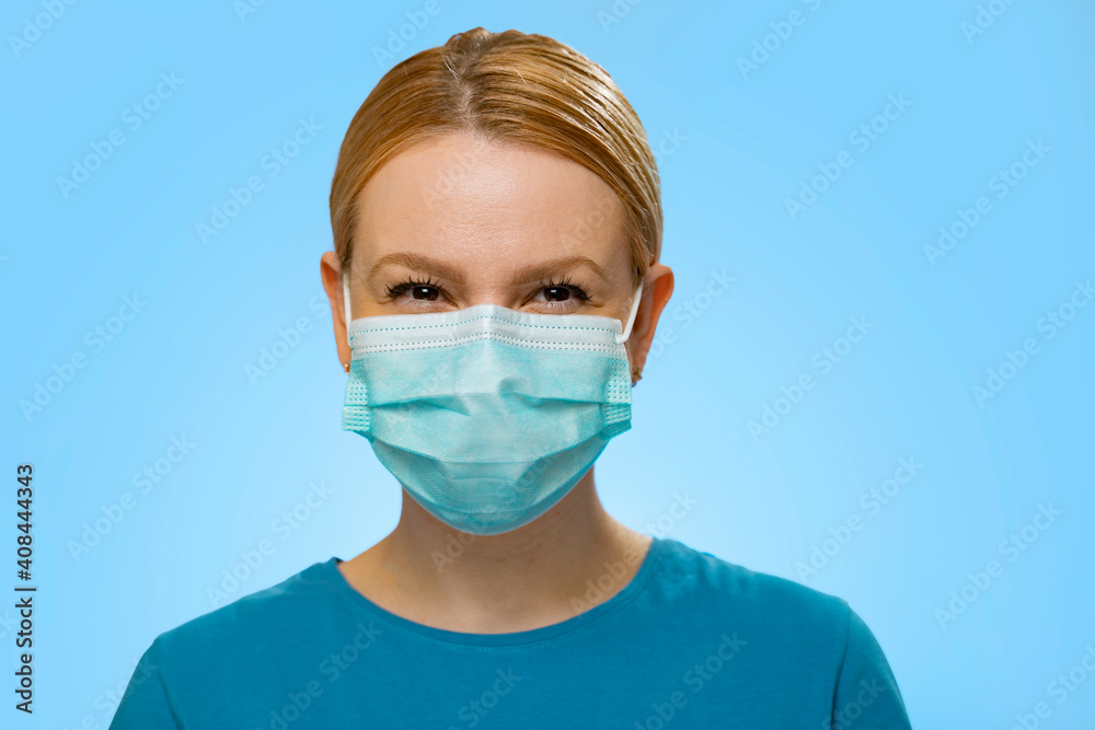 Charismatic , happy woman with surgical mask on , smiling under the mask . Medical personnel or civilian on blue background Charismatic , happy woman with surgical mask on , smiling under the mask . Medical personnel or civilian on blue background