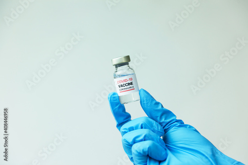 Hand of doctor with blue nitrile glove holding a COVID-19 coronavirus vaccine vial on white background