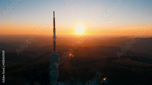 Cinematic aerial shot of golden sunset in background and Tv Tower Silhouette in foreground on top of mountain. Slow steady wide shot.  photo