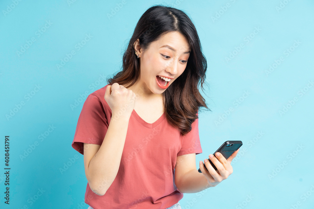 The beautiful Asian woman is looking at her phone and showing a triumphant expression The beautiful Asian woman is looking at her phone and showing a triumphant expression