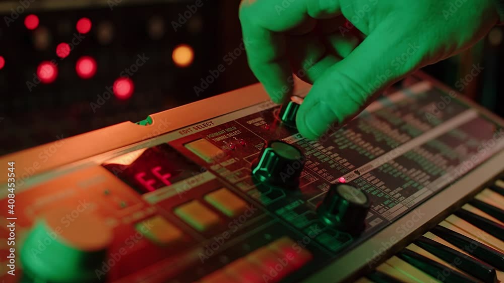 close up slow motion shot of a man playing keys and turning knobs on a vintage synth, red and green mood