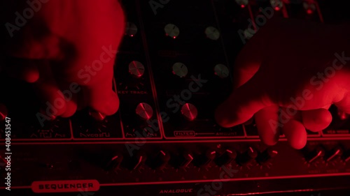 slow motion macro shot of a man turning knobs on a vintage synth, dark red and green ambiance photo