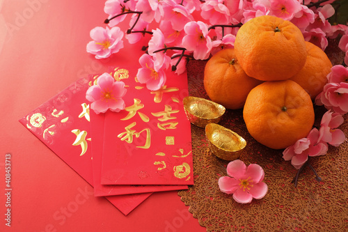 Chinese New Year festival concept. Mandarin oranges, red envelopes, and gold ingots on red background decorated with plum blossom. Chinese character 