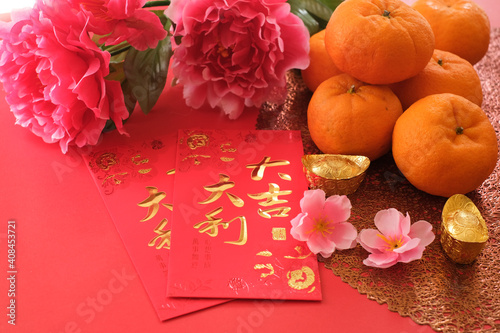 Chinese New Year festival concept. Mandarin oranges, red envelopes, and gold ingots on red background decorated with pink peony. Chinese character 