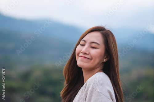 Portrait image of a beautiful young asian woman close her eyes while standing in front of the mountains outdoors