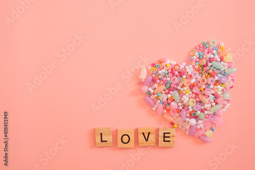 Colorful heart shape made of beads as a symbol of love with letter words of “LOVE” isolated on pastel light pink background. Valentine’s day, gift, message of lover, greeting card. Love concept.