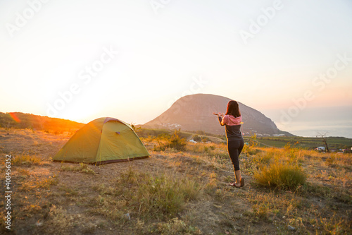 Woman meets the dawn in the mountains  rejoices in the sun. Panoramic view of the mountain and the sea from above. Camping  outdoor activities  sports mountain hiking  family travel. Ayu-Dag  Crimea.