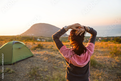 Woman meets the dawn in the mountains, rejoices in the sun. Panoramic view of the mountain and the sea from above. Camping, outdoor activities, sports mountain hiking, family travel. Ayu-Dag, Crimea.