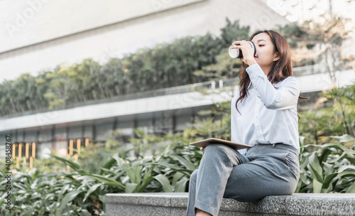 woman sitting on a bench in park is drinking coffee