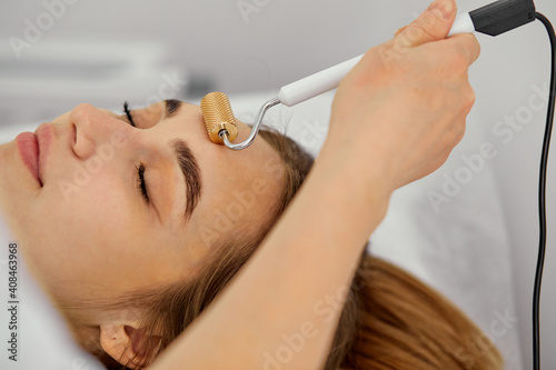 facial madero massage with a face roller, young woman in beauty salon close up get procedures by professional medical workers comsetologists