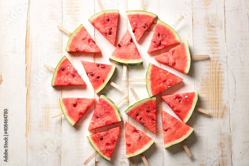 Slices of ripe watermelon with sticks on wooden background