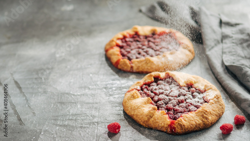 Raspberry galette with copy space. Powdered sugar poured onto delicious rustic homemade tart with frozen or fresh raspberries on gray background