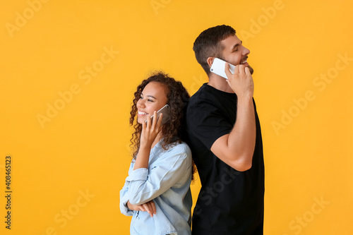 Young couple talking by mobile phones on color background