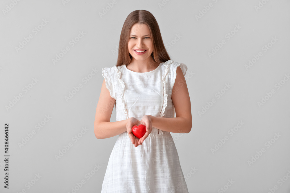 Young woman with red heart on grey background Young woman with red heart on grey background