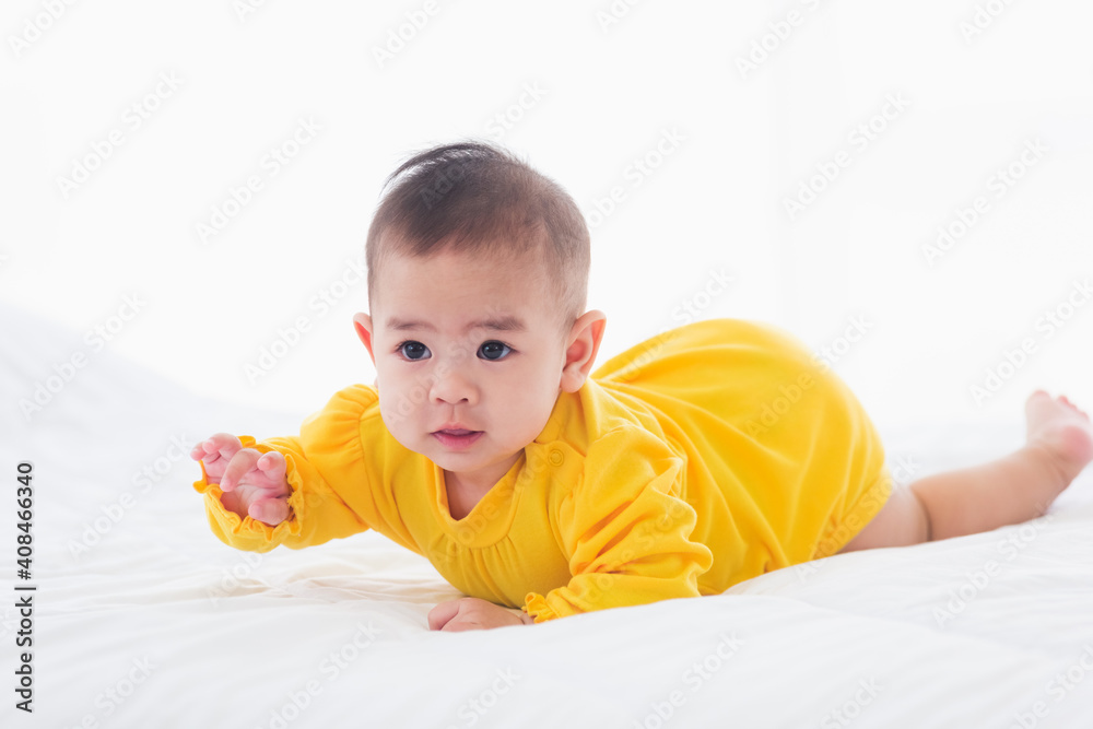 Portrait of beautiful young Asian newborn little baby prone on the bed at home, Happy baby smile wears a yellow shirt relaxing in the room, Family morning at home Portrait of beautiful young Asian newborn little baby prone on the bed at home, Happy baby smile wears a yellow shirt relaxing in the room, Family morning at home