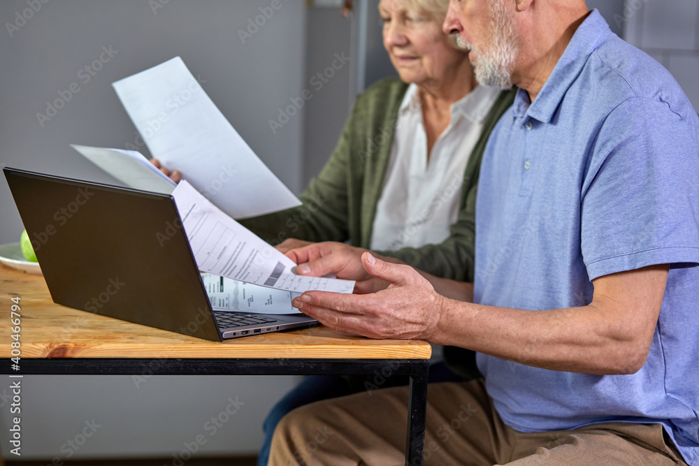 cropped elderly man and woman managing family monthly budget together, focused married couple using computer banking application, counting bills in the kitchen. focus on laptop and hands cropped elderly man and woman managing family monthly budget together, focused married couple using computer banking application, counting bills in the kitchen. focus on laptop and hands