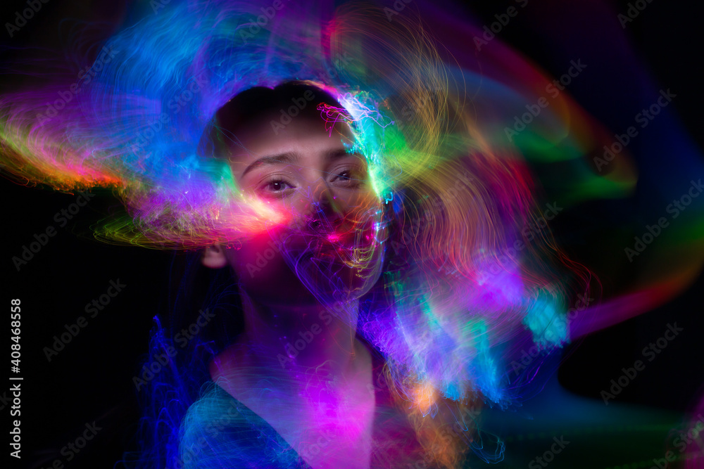 Fototapeta premium Portrait of young woman amid light painting , Over Black Background. Long exposure photo without photoshop, light drawing at long exposure