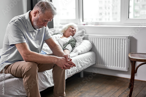 elderly man crying and mourning the loss of his wife, sitting by her side. coronavirus, covid-19 concept