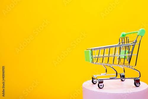 Metal mini shopping trolley on pink podium isolated on a yellow background, shopping symbol. Sales concept with copy space