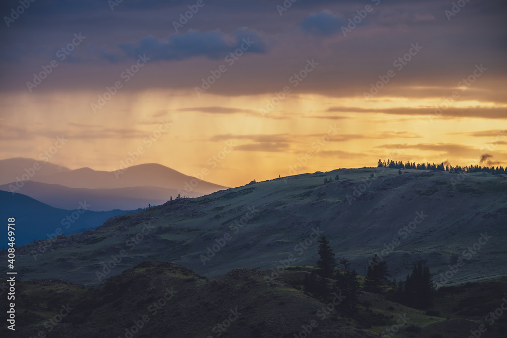 Atmospheric landscape with silhouettes of mountains with trees on background of vivid orange blue violet dawn sky. Colorful nature scenery with sunset or sunrise of illuminating color. Sundown paysage