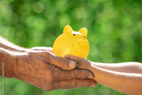 Fotografie Family holding piggy bank in hands against green spring background